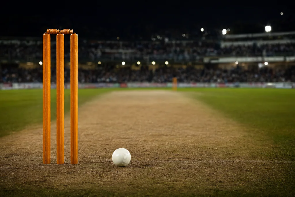 Cricket stumps and a white ball on a floodlit pitch at night