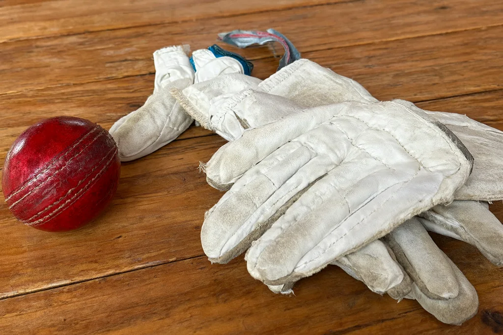 A cricket ball beside batting gloves on a wooden table