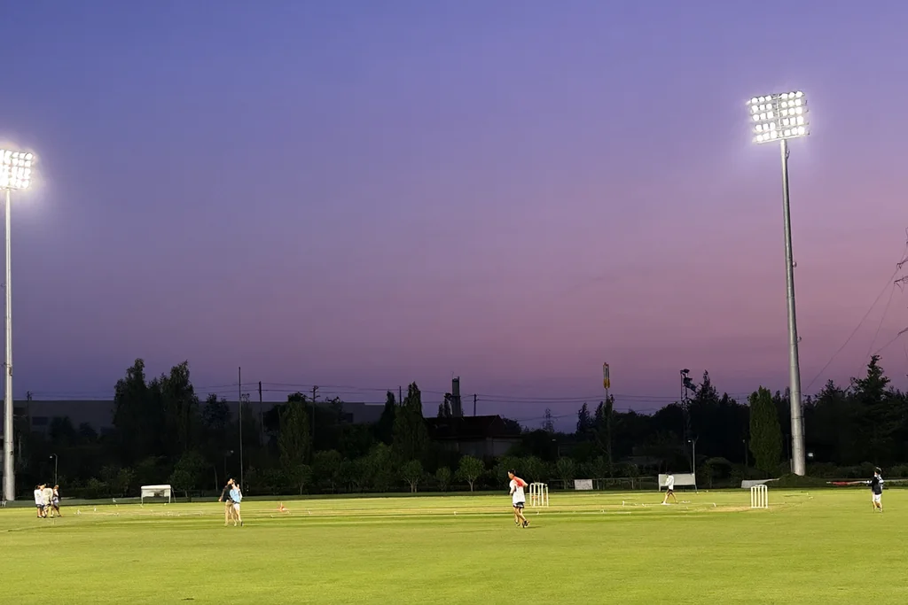 Floodlight towers above an empty cricket ground at dusk