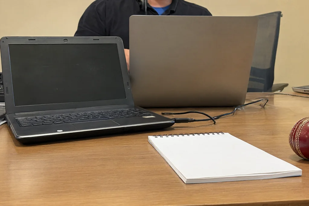 An analyst desk with a closed laptop, a notepad and a cricket ball