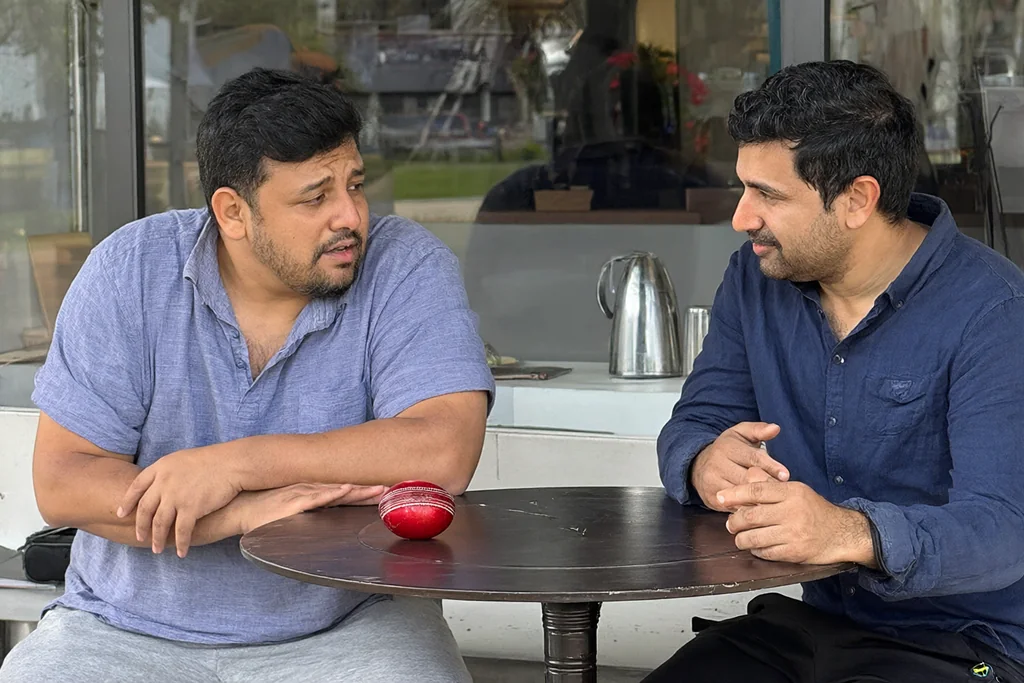 Two cricket fans discussing a match at a table with a cricket ball