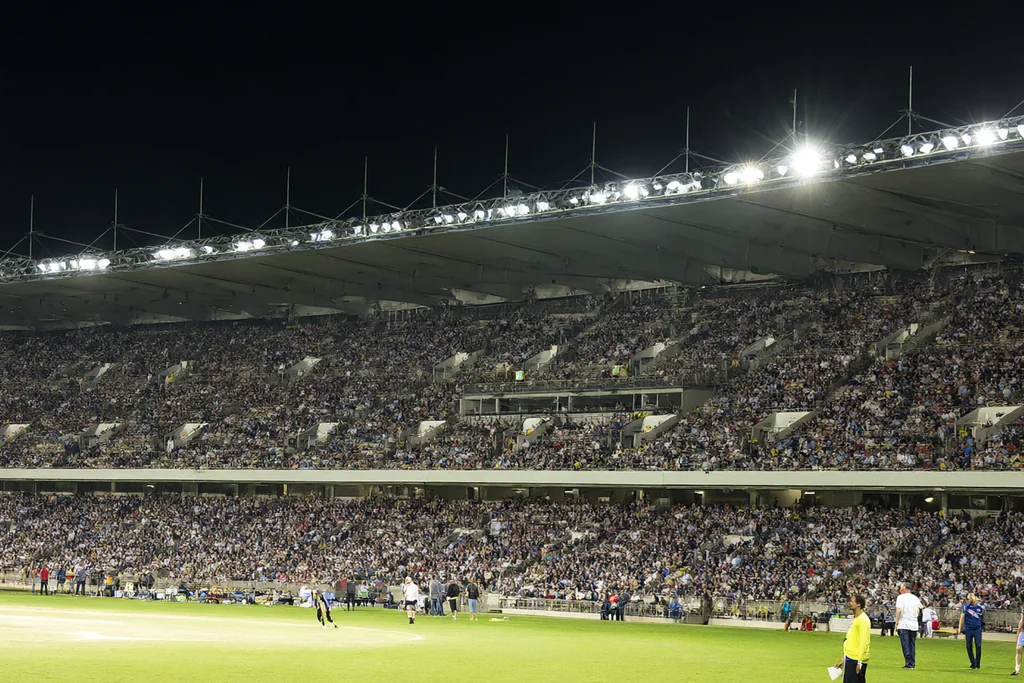 A cricket stadium packed with spectators under floodlights